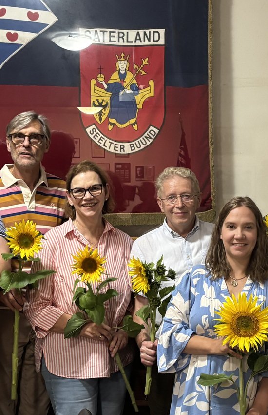 Zu sehen sind drei Kreisvorstandsmitglieder und die vier frisch gewählten Ortsvorstandsmitrglieder mit Sonneblumen in den Händen vor dem Saterländer Wappen hinter Glas.