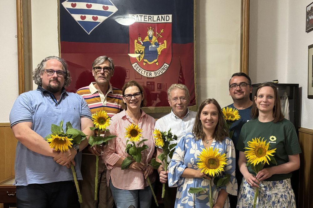 Zu sehen sind drei Kreisvorstandsmitglieder und die vier frisch gewählten Ortsvorstandsmitrglieder mit Sonneblumen in den Händen vor dem Saterländer Wappen hinter Glas.
